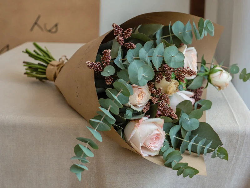 Bouquet de roses de jardin, renoncules et eucalyptus en papier kraft sur un plan de travail en lin.