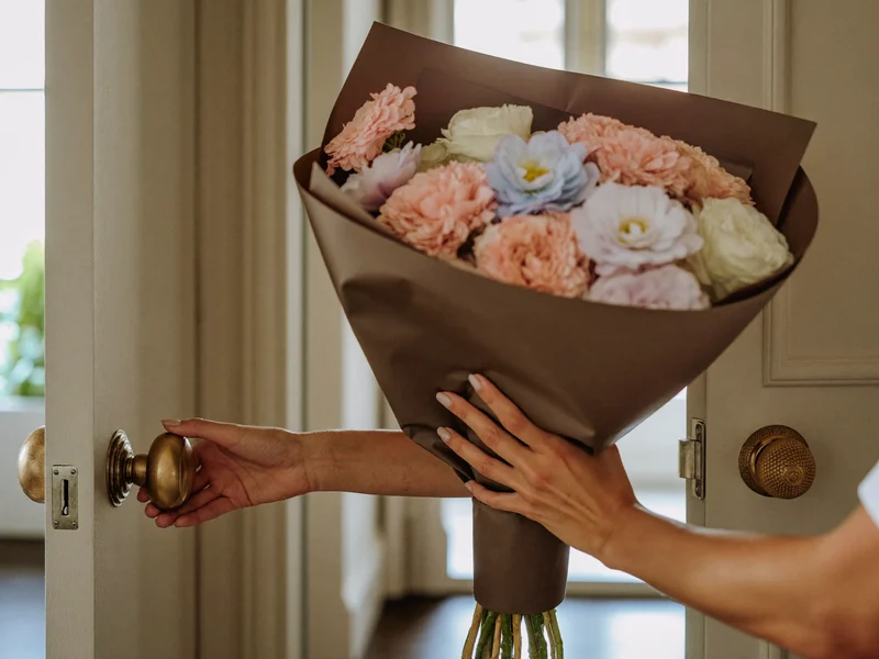 Remise d'un bouquet emballé de papier à la porte ouverte d'un appartement français.